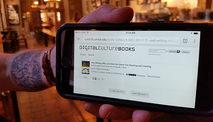 Close-up of a human hand holding a mobile device with the homepage for Digital Culture Books on the screen.